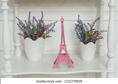 A pink statuette in the shape of the Eiffel tower on a shelf with vases of lavender. Miniature Eiffel tower souvenir decor of the interior. Beautiful artificial lavender in the interior of shabby chic