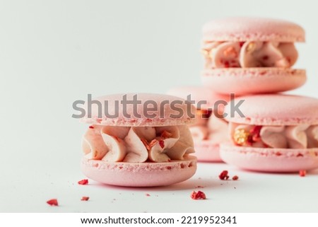 Pink strawberry macaroons decorated with golden petals and freeze-dried red berries stacked together in a pile. Traditional French dessert. White background. Close up shot.