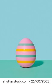 Pink striped Easter egg in 80s-90s retro style. A pink egg with multi-colored stripes on a two-tone background of mint and blue hues. Happy Easter vintage card.