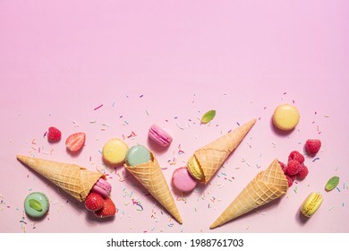 Pink summer background idea. Colorful dessert ice cream waffle cone with pastel macarons, strawberries and raspberries