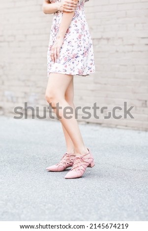 Pink Summer Outfit -
A fashionable woman wearing a floral dress stands on a sidewalk.