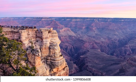 A pink sunset pours over a crowd of visitors enjoying the canyon views from Mather Point in Grand Canyon National Park, Arizona.
