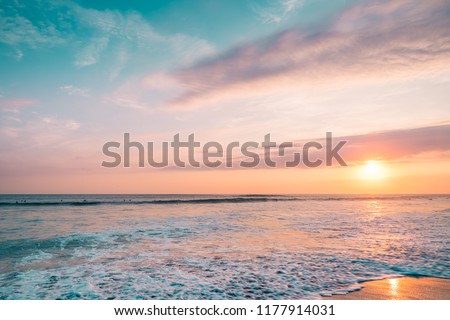 Pink Sunset Sea with Surfers.  Colorful Landscape of Paradise Tropical Island Beach, Sunrise Surfing Shot. Blue & Pink Barrel Wave in Ocean. Clear Surfers Wave and Sun Light. Ocean Water Background.