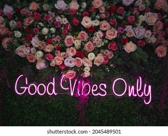 Pink text shaped Good Vibes Only neon lights below the shades of red roses in a cafe at Suka Bakti ward, Tangerang city.