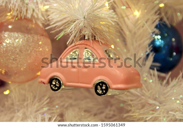 pink toy car against the background of\
branches of white artificial spruce and pink glass New Year ball.\
Christmas background decor and\
decorations