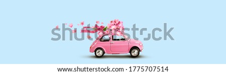 Pink toy car with bouquet of flowers on a roof with ribbon and bow on blue background. Flowers delivery.