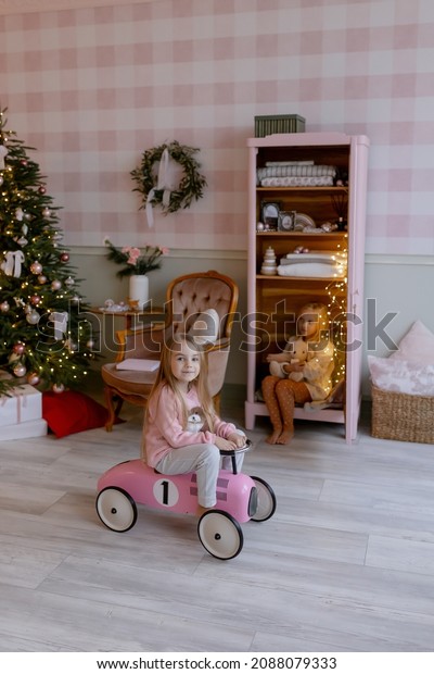 Pink toy car Child sits on the background of the\
Christmas tree in the room