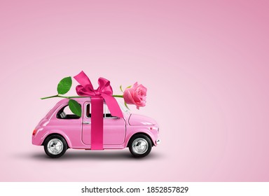 rosafarbene Spielzeugautos mit rosafarbener Rosenblume und rosafarbenem Hintergrund. Valentinstag, Blumenverleih, Frauentag. Platz für Text.