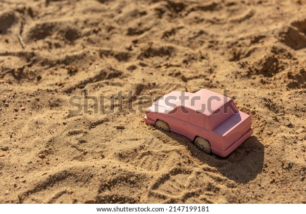 Pink toy car in the\
sand at a playground.