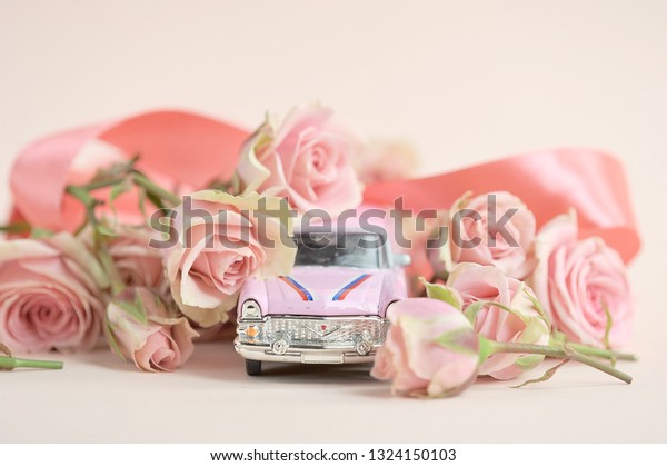 Pink toy\
car surrounded by a bouquet of spray roses. The concept of holiday\
greetings. Close-up. Light\
background.