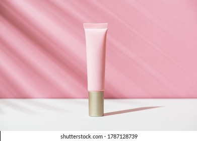 Pink Tube Of Soft Organic Natural Eye Cream With Golden Cap On White Pink Background, Palm Leaf Shadow. Summer Facial Product, Sun Lotion. Women's Hygiene Cosmetic Accessory For Skincare. Copy Space.