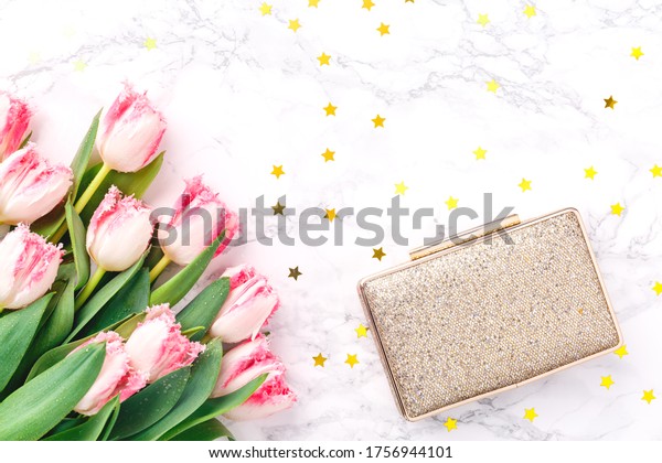 Pink tulips and golden evening clutch on white\
marble background. Spring and celebration concept. Copy space Top\
view. Horizontal
