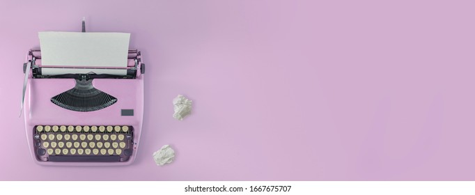 A pink vintage typewriter with pink background and two paper balls. 
