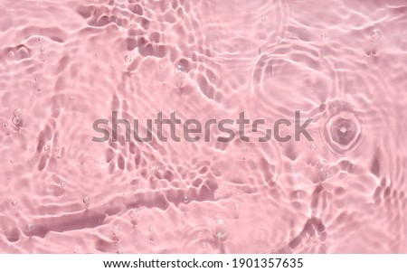 Pink water texture with ripples, waves and bubbles. Closeup of sun reflections and shadows on textured water surface. Trendy abstract summer background with rippled swimming pool