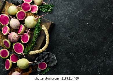 Pink watermelon radish lying on a couple of whole light green watermelon radishes. On a black stone background. - Shutterstock ID 2199214469
