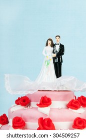 Pink wedding cake with red roses and couple on top on blue background