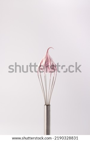 Pink whipped cream made from protein and sugar on a whisk. Marshmallow or raspberry meringue. Whisk with cream on a white background. 