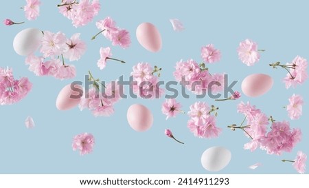 Pink and white Easter eggs adorned with cherry blossom branches, levitating against a blue background. Easter themed Springtime nature decoration concept.	