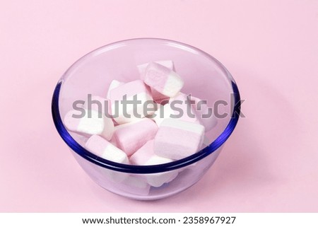Pink and white marshmallow cubes in a blue glass bowl on a pink background