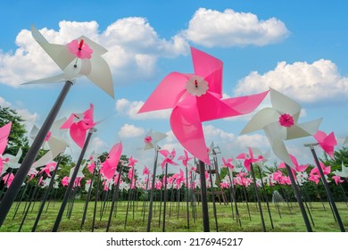 Pink And White Plastic Windmills Toy On Green Grass And Blue Sky Background. Small Plastic Colorful Turbine And White Cloud, Pin Wheel In Nature