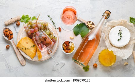 Pink wine rose aged cheese Camembert cheese nuts honey red grapes glasses of wine. Delicious food wine snacks assorted served on boards. Flat lay long web banner on light gray concrete background.