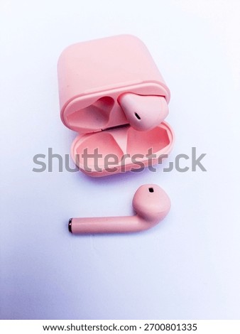 A pink wireless earbud charging case is open, showing one bud inside. The second matching pink earbud rests nearby on a white surface..
