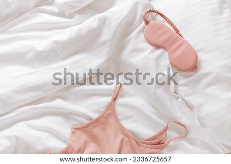 Pink woman pajamas and sleep eye mask on bed. Top view summer pyjama for sleeping. Aesthetic lifestyle flat lay photo, singlet and shorts peach colored, comfort ans stylish wear or clothes, copy space