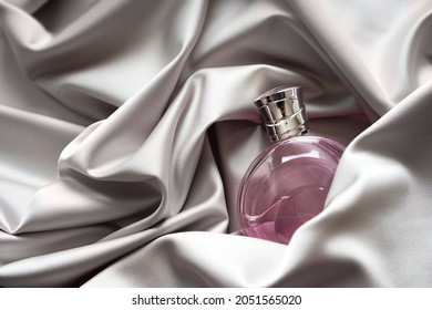 Pink women's perfume bottle in satin cloth draperies.