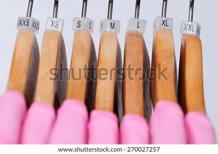 Pink women's t-shirts hang on wooden hangers with indexes of the XXS, XS, S, M, L, XL, XXL sizes on a light background.