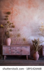 a pink wooden chest of drawers stands near a pink wall. On the chest of drawers there are vases of dried flowers. Interior design concept, flowers in the interior, color combination
