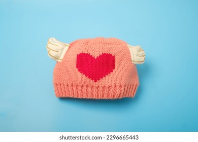 Pink wooly beanie hat for baby, toddlers and young kids isolated on blue color background. Handmade woolly cap decorate with red heart shape, Baby shower concept - Powered by Shutterstock