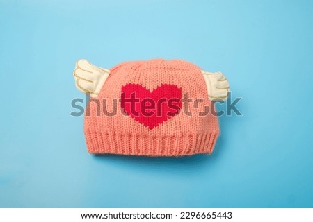 Pink wooly beanie hat for baby, toddlers and young kids isolated on blue color background. Handmade woolly cap decorate with red heart shape, Baby shower concept