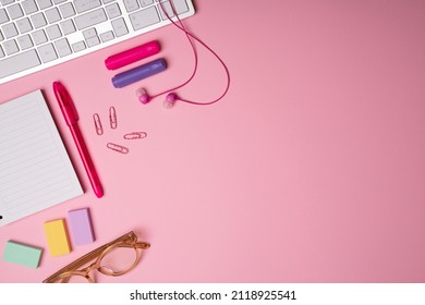 Pink workspace. Flat lay of a woman's office desk with her earphones, glasses, notepad, pens and markers next to copy space 