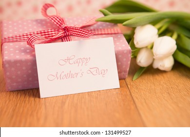 Pink Wrapped Present With Bunch Of White Tulips And Mothers Day Card On Wooden Table