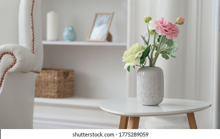 Pink and yellow roses in Modern white vase on white table beside classic armchair