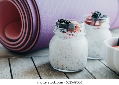 Pink yoga mat and Pudding with chia seeds, yogurt and fresh fruits: Strawberries, blueberries and blackberries in glass jars on wooden background
