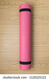 Pink Yoga Or Pilates Mat On Wooden Floor. Equipment For Healthy Lifestyle And Diet. Rolled Up. Preparing For Exercise. Top View.