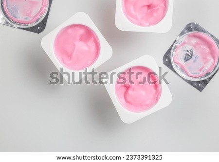 Pink yogurt cup - top view of strawberry yoghurt in plastic cups with foil lids on white background with copy space