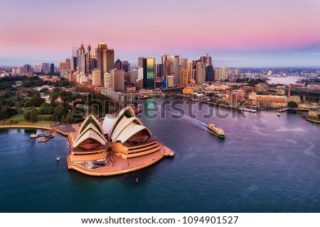 Pinkish colourful sunrise over Sydney city CBD on waterfront of Harbour around Circular quay with major architectural landmarks and symbols of Australia.