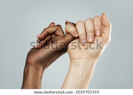 A pinky promise gesture between African and Caucasian women. Closeup of palms on gray background. Interracial friendship, care and support.