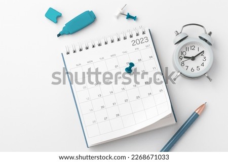 Pinned date on calendar 2023 with stationery on white table, top view