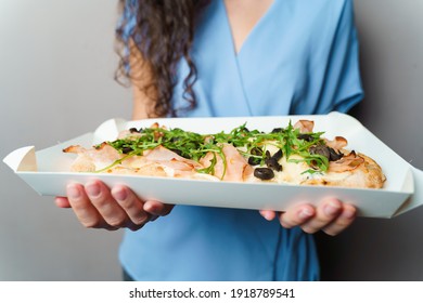 Pinsa Romana In White Delivery Box. Courier Holding Crocchiarella Gourmet Italian Cuisine On White Background. Food Delivery From Pizzeria. Pinsa With Meat, Arugula, Olives, Cheese.