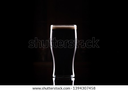 Pint Glass of Black Stout Beer with black background and reflection on bar