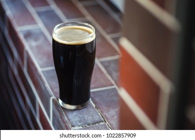 Pint Glass Of Dark Stout Beer Standing On A Grunge Brick Windowsill