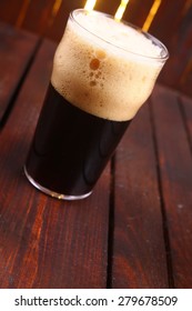 A Pint Glass Full Of Dark Stout Ale Standing On A Wooden Table