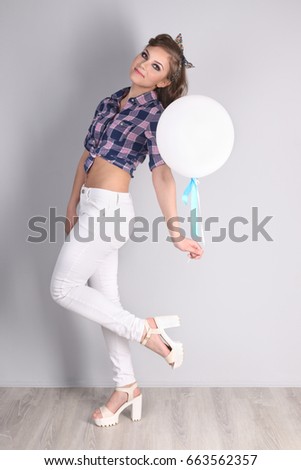 Pinup girl in checkered shirt and pants poses with balloon in studio