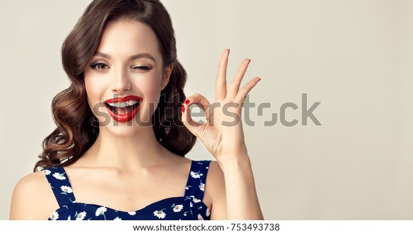 Pin-up retro girl with curly hair  winking,\
smiling and showing OK sign . Presenting your product. Expressive\
facial expressions\
