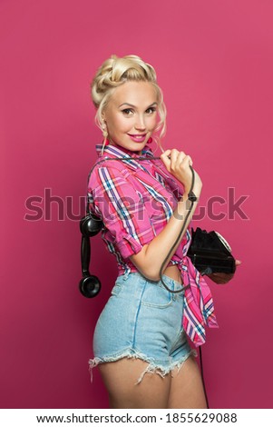 Pin-up woman smiling and holding retro phone on pink background