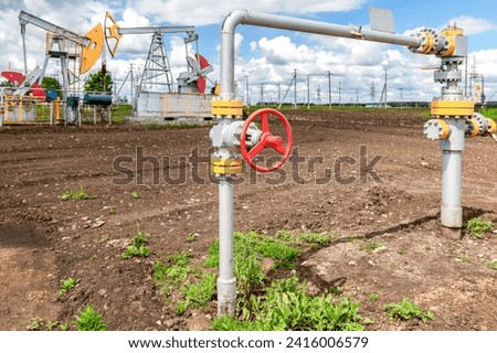 Pipe with control valve against the background pump jack fracking crude oil extraction machine. Oil industry equipment and business concept