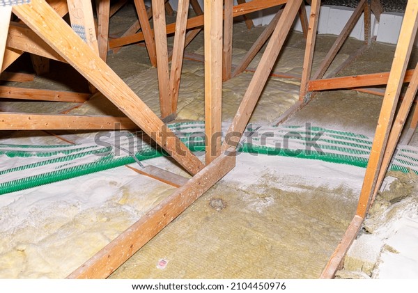 Pipe insulation with expanded perlite in\
domestic ventilation with energy recovery, a visible system of\
green pipes spread over the roof\
trusses.